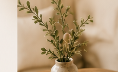 A small vase of olive branches on a wooden table in a warm, softly lit room